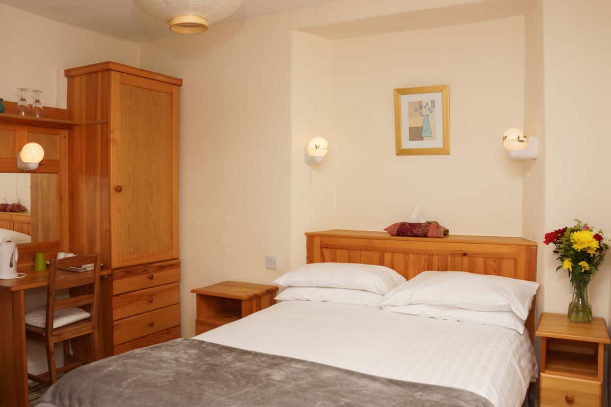 A bedroom with a wooden bed, bedside tables, a wooden wardrobe, and a wall-mounted light fixture.