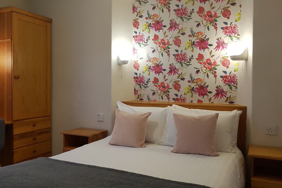 A hotel room with a bed, bedside tables, a wardrobe, a mirror, and floral wallpaper.