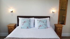 A neatly made bed with floral pillows, two bedside tables, and wall-mounted lights. - The Old Courthouse (Windermere)