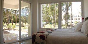 A bedroom with a large bed, a view of a garden through a sliding glass door, and a balcony. - Green Park Punta 2 (Punta Ballena)