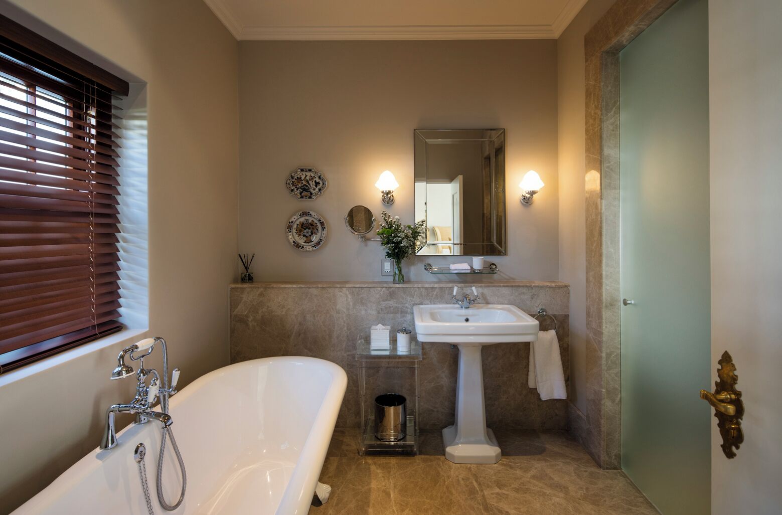 A bathroom with a freestanding bathtub, a pedestal sink, and a vanity mirror.