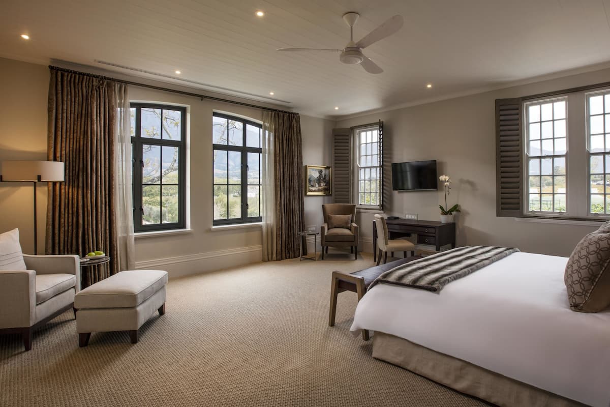 A spacious bedroom with a large bed, a desk, a chair, and a television.
