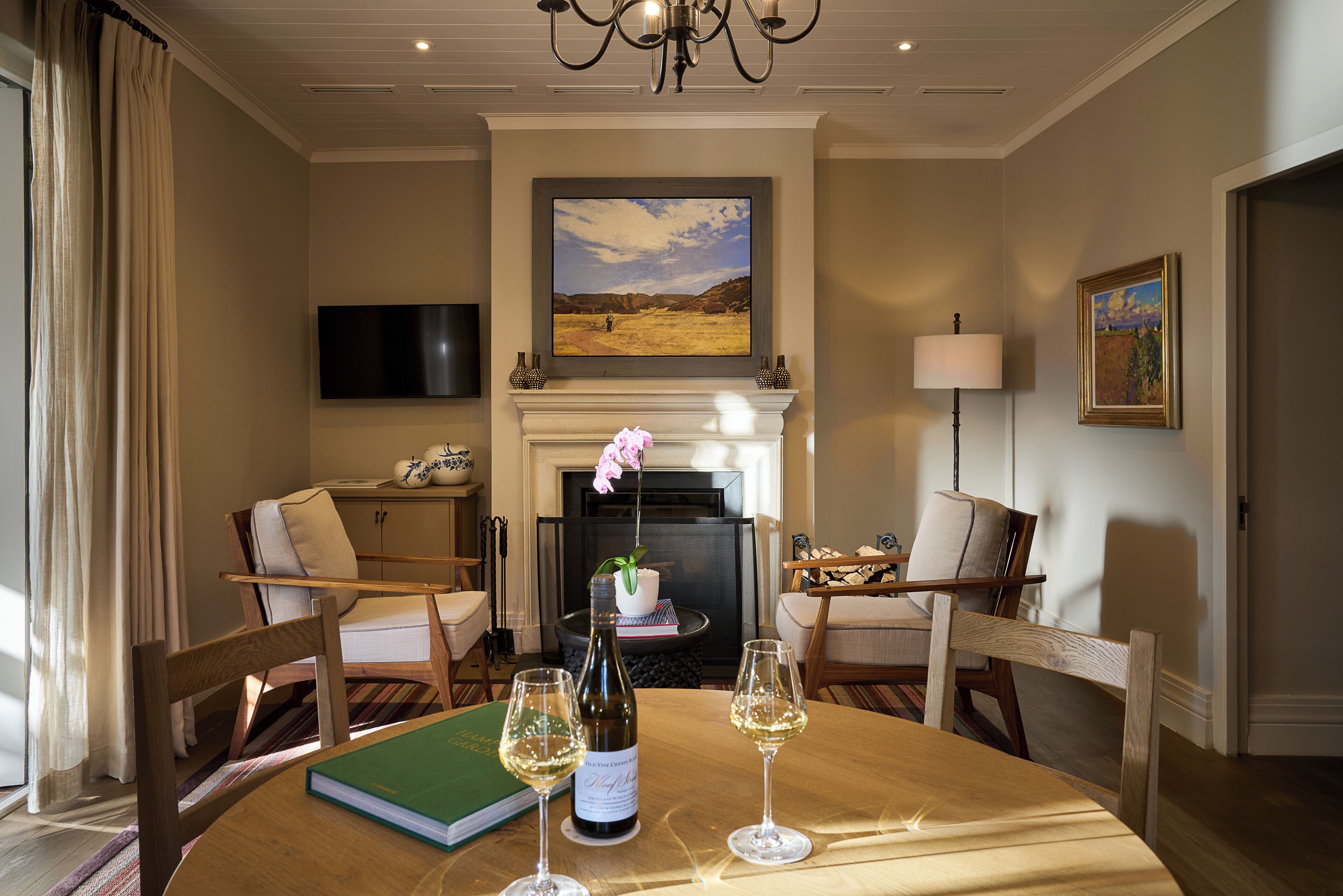 A cozy living room with a fireplace, comfortable seating, a television, and a table with wine glasses and a book.