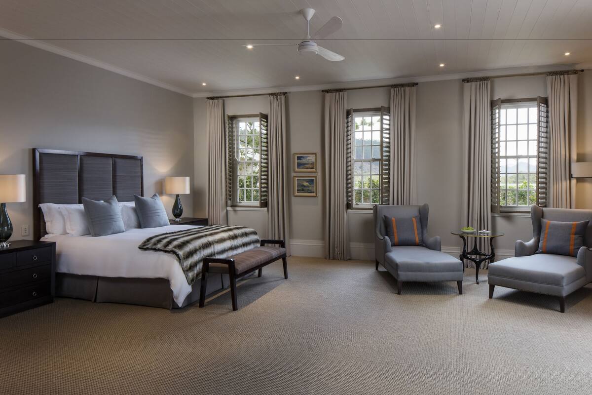 A hotel room with a bed, two armchairs, a small table, and a ceiling fan.