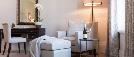 Un salon moderne comprenant un canapé, un fauteuil et un pouf, un bureau avec une chaise, un grand miroir, une lampe sur pied et un vase orné d’une orchidée.