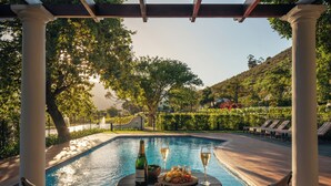 A poolside setting with a table, two chairs, a bottle of champagne, and glasses. - Leeu Estates (Franschhoek)