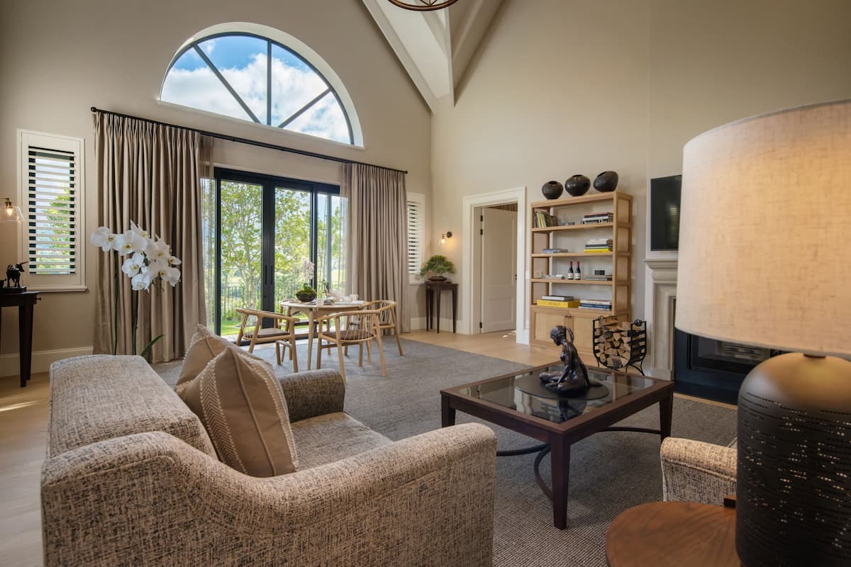 A spacious living room with a large window, a cozy seating area, and a bookshelf.
