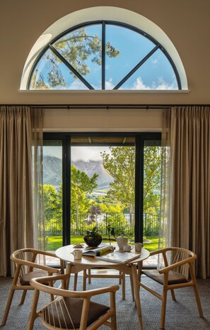 A dining area with a table and chairs, a window with a view of greenery and mountains, and a large arched window above.