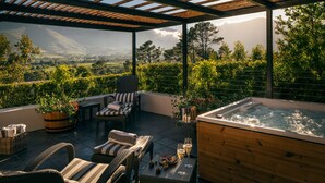 A terrace with wicker furniture, a hot tub, and a view of a mountainous landscape. - Leeu Estates (Franschhoek)