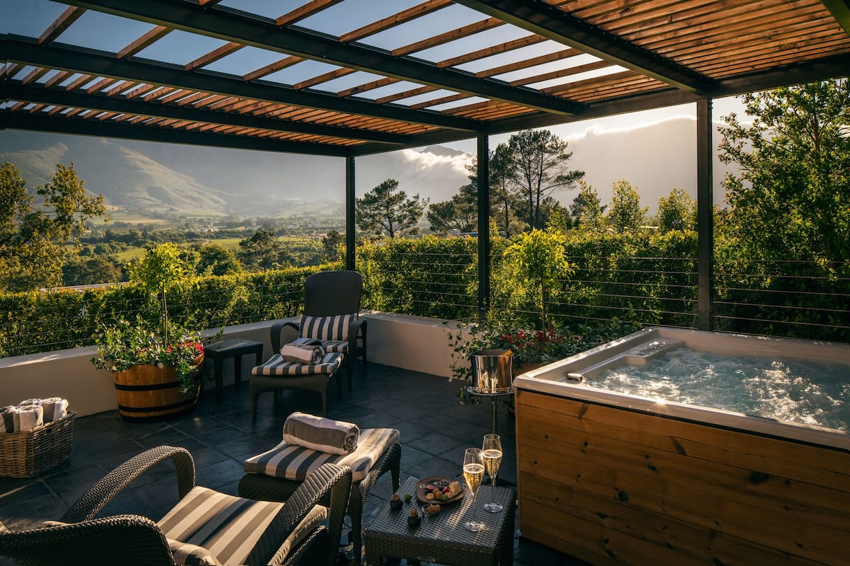 A terrace with wicker furniture, a hot tub, and a view of a mountainous landscape.