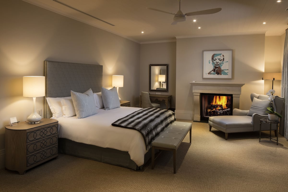 A spacious bedroom with a large bed, bedside lamps, a fireplace, a sofa, and a ceiling fan.
