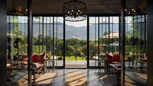 A spacious room with large windows, a chandelier, and a view of mountains. - Leeu Estates (Franschhoek)