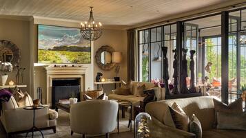 A cozy living room with a fireplace, comfortable seating, and large windows offering a view of the outdoors.