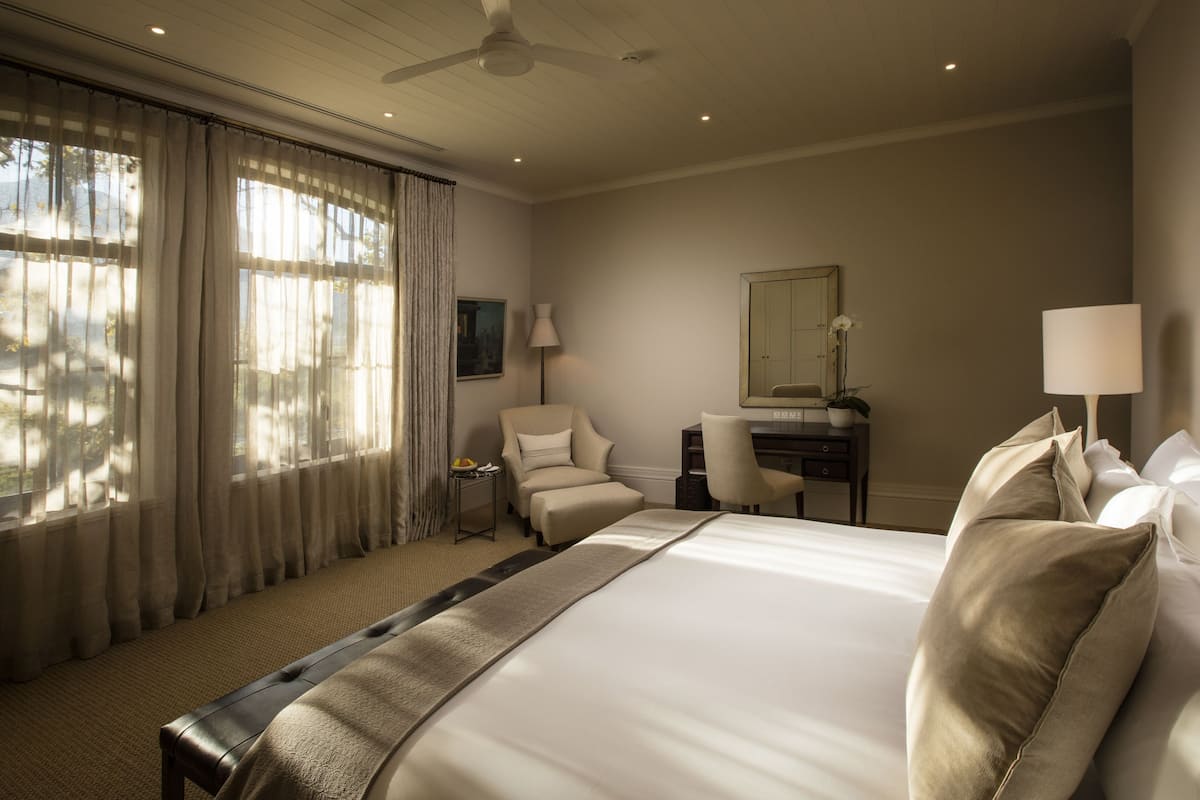 A hotel room with a large bed, a desk, a chair, and a ceiling fan.