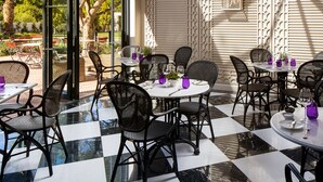 Een eetruimte met geruit vloerkleed, zwarte rieten stoelen en gedekte tafels.