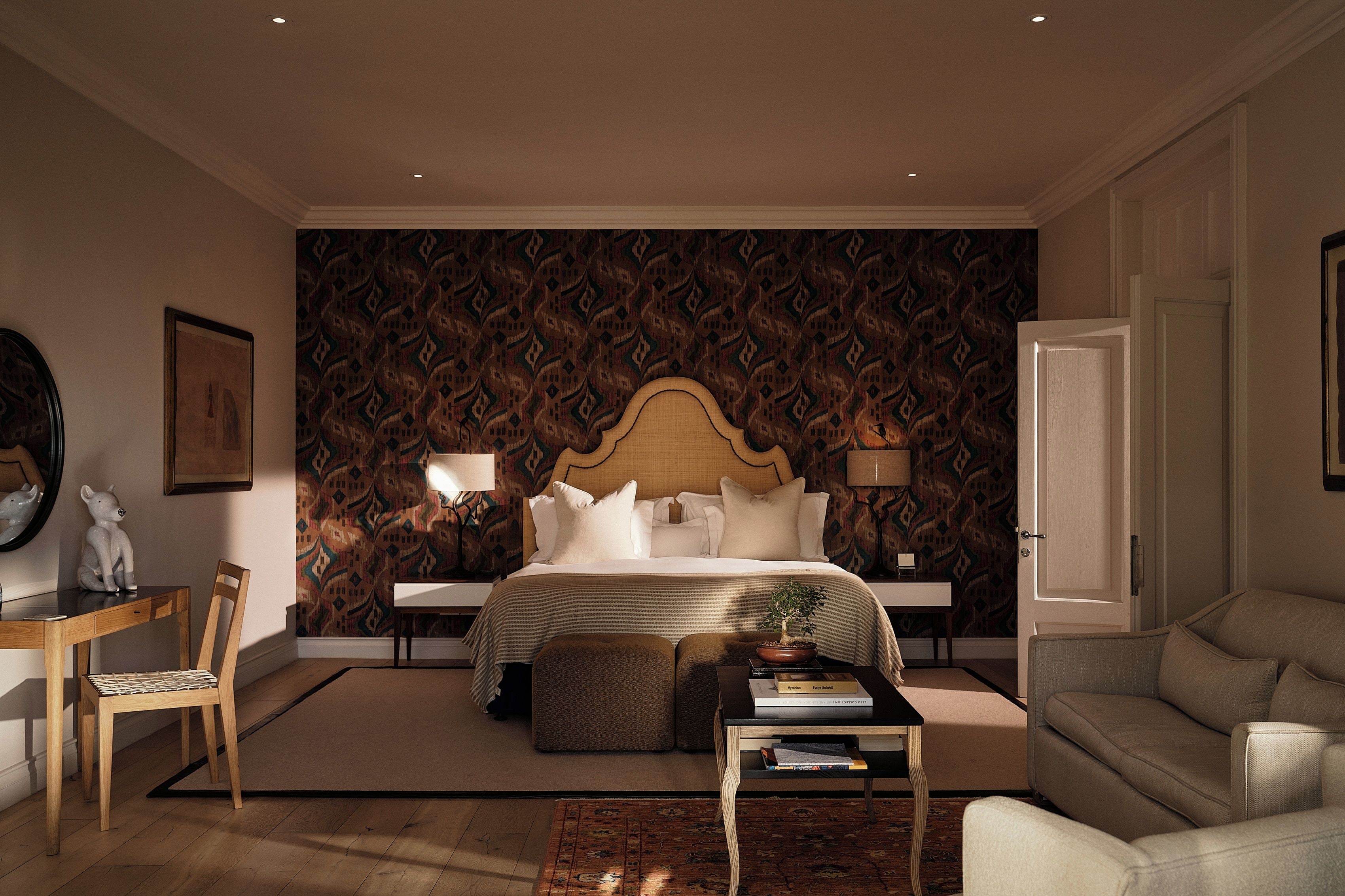 Ein Schlafzimmer mit einem großen Bett, Nachttischen, einem Sessel, einer Couch, einem kleinen Tisch mit einer Pflanze und einer gemusterten Tapete.