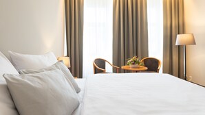 Ein Hotelzimmer mit einem Bett, zwei Stühlen, einem kleinen Tisch mit Blumenvase und Vorhängen.