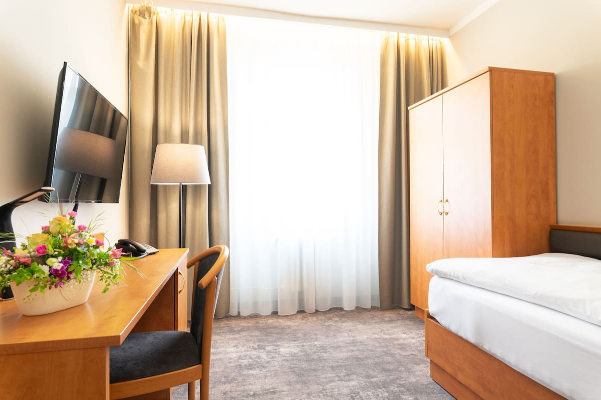 A hotel room with a bed, a desk with a lamp, a TV, and a wardrobe.