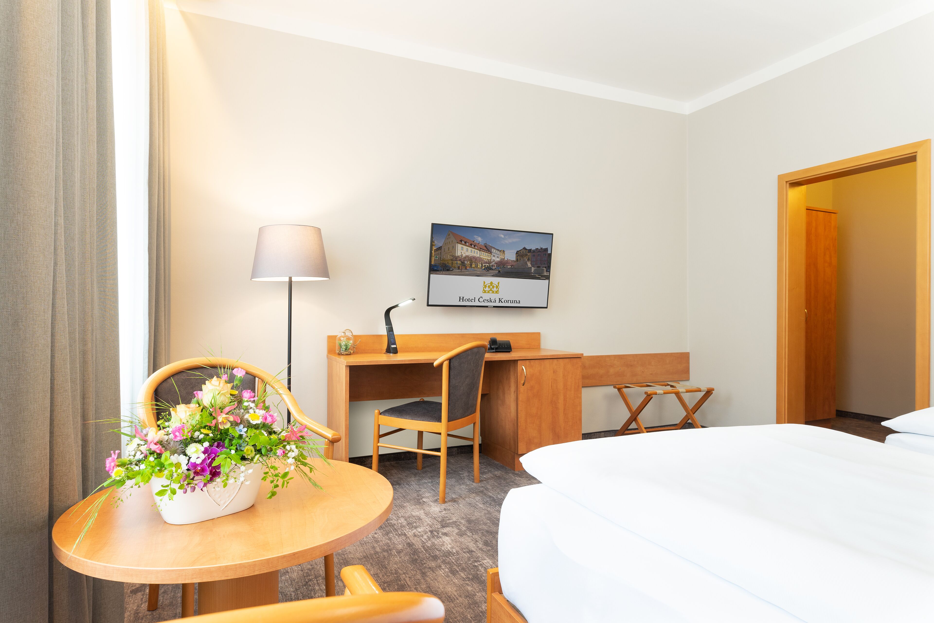A hotel room with a bed, a desk with a chair, a lamp, and a framed picture on the wall.
