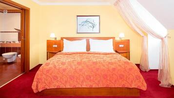 Habitación de hotel con una cama, dos mesitas de noche, un tocador, un cuadro enmarcado en la pared y un baño visible a través de una puerta abierta.