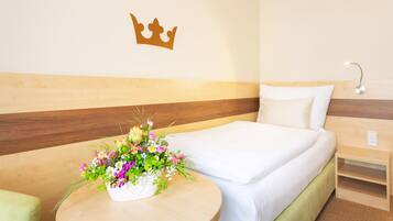 A hotel room with a bed, a nightstand, a wall-mounted crown decoration, and a floral arrangement on the nightstand.