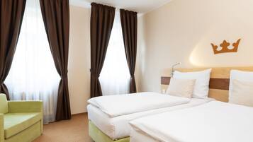 A hotel room with two beds, a green armchair, and a crown decoration on the wall.