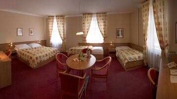 Une chambre d’hôtel avec deux lits simples, une petite table ronde avec des chaises, un bureau avec une chaise et un téléphone.