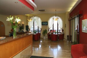 Un vestíbulo de hotel con mostrador de recepción, zona de estar y grandes ventanales con cortinas.