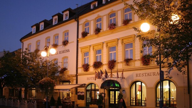 Ein Hotel im klassisch europäischen Stil, mit Rundbogenfenstern und einem Schild, auf dem 'HOTEL KORUNA RESTAURANT' steht.