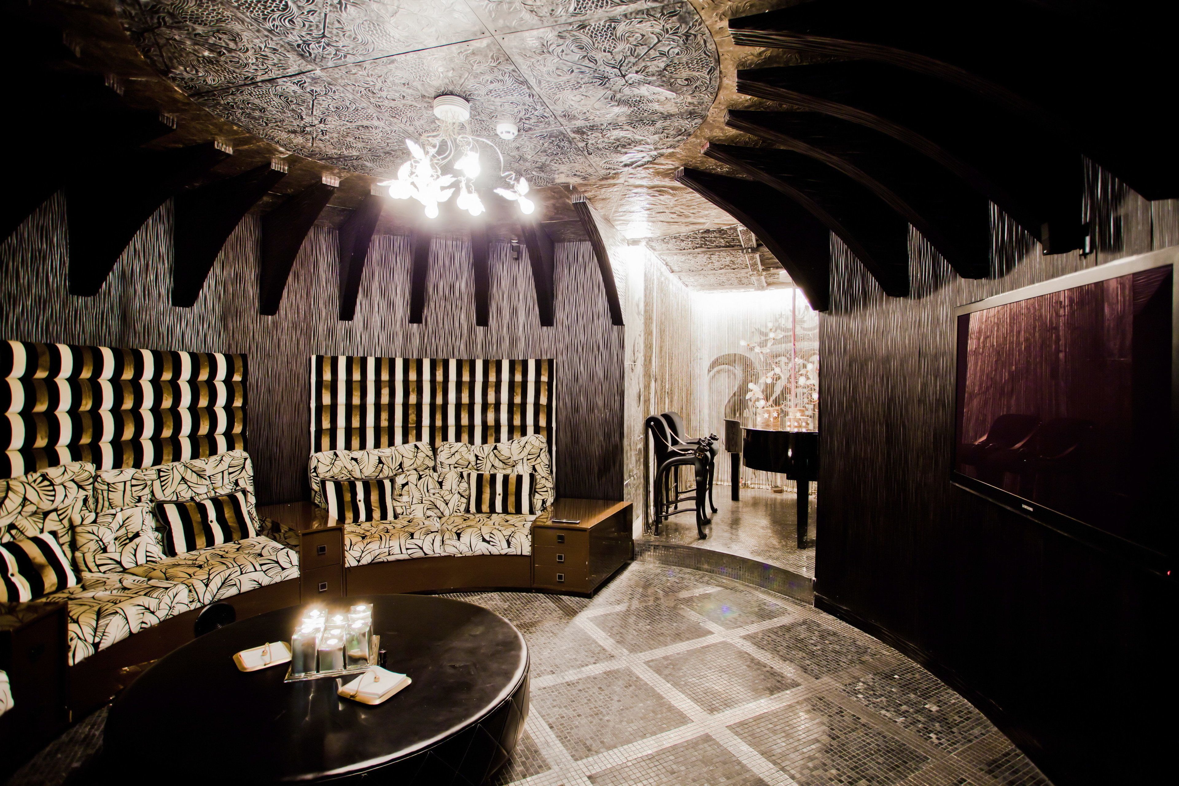 A dimly lit room with a patterned sofa, a round table with candles, and a chandelier.