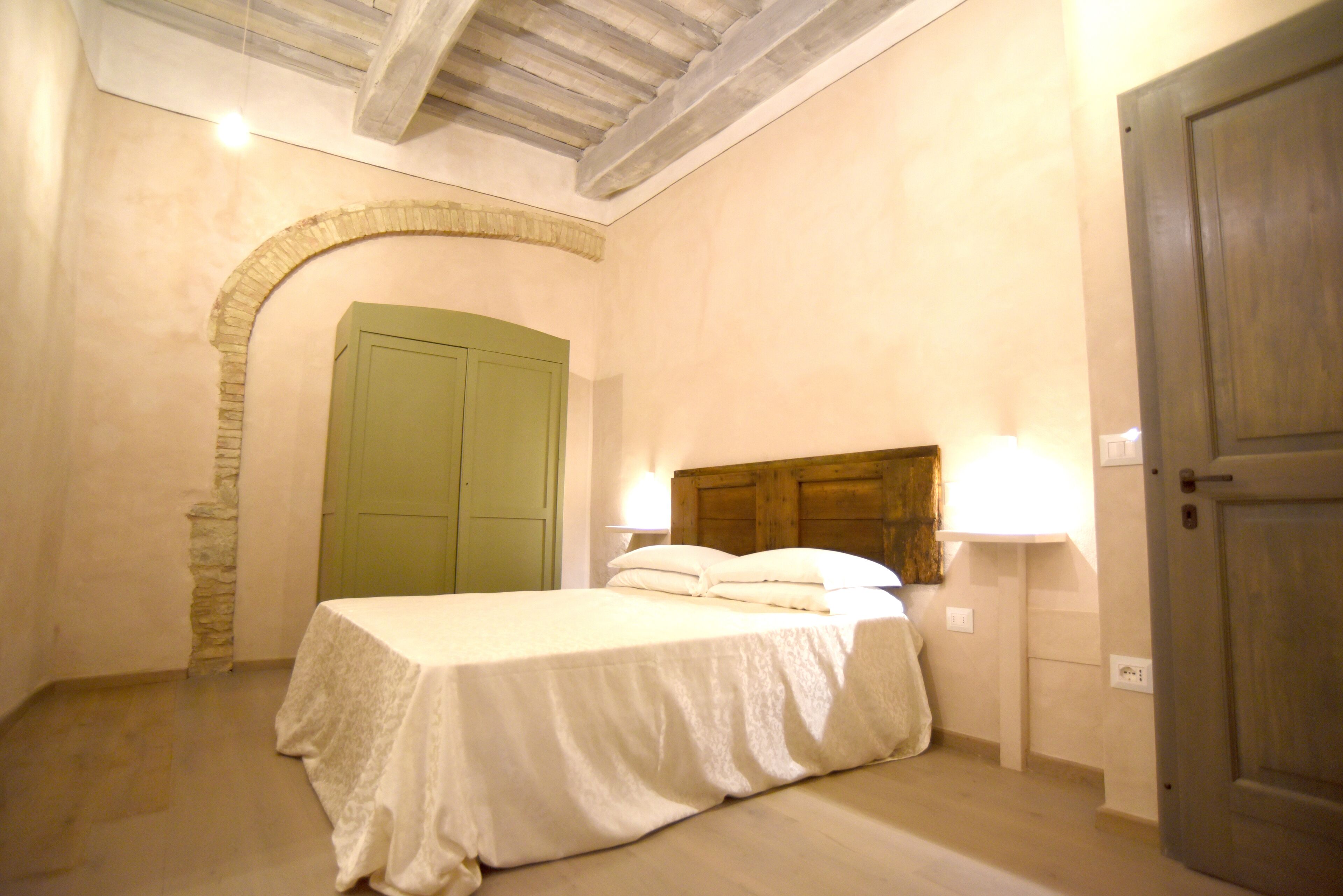 Une chambre à coucher avec un lit, une porte verte, un mur en pierre et un plafond en bois.