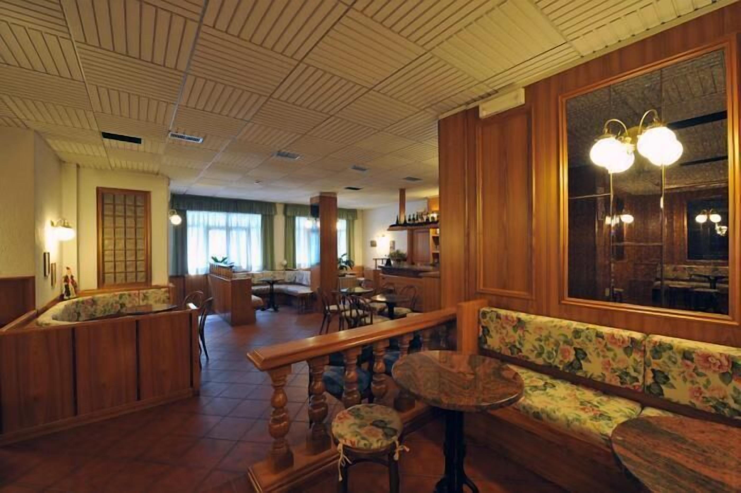 Un hall d’hôtel spacieux, doté de boiseries, d’un grand miroir et d’un coin salon avec des meubles recouverts d’un tissu à motifs floraux.