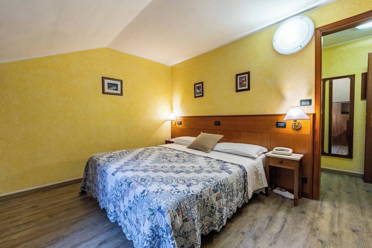 Una habitación de hotel con cama, mesitas de noche y cabecera de madera.