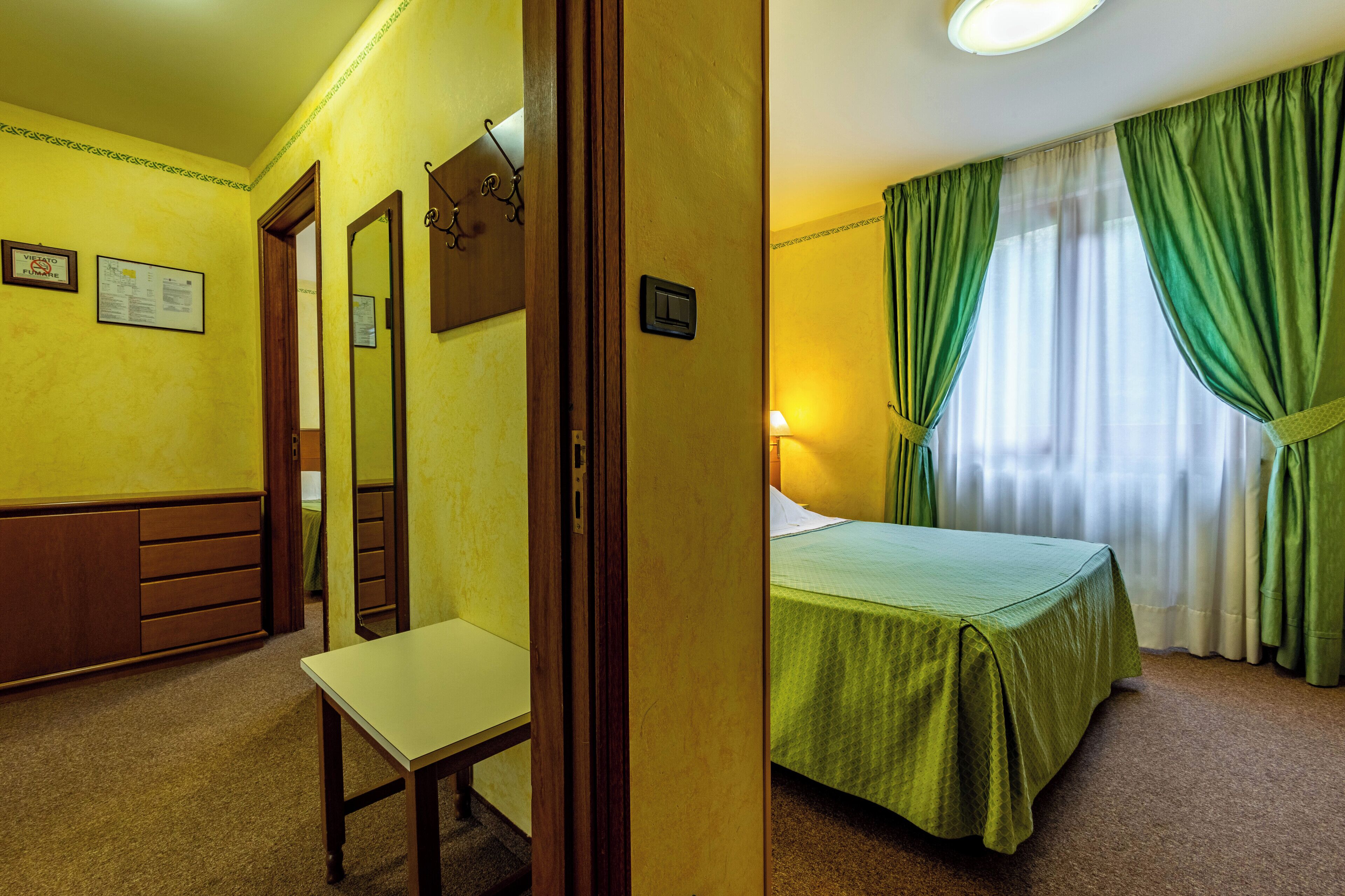 A hotel room with a bed, a desk, a mirror, and a door.