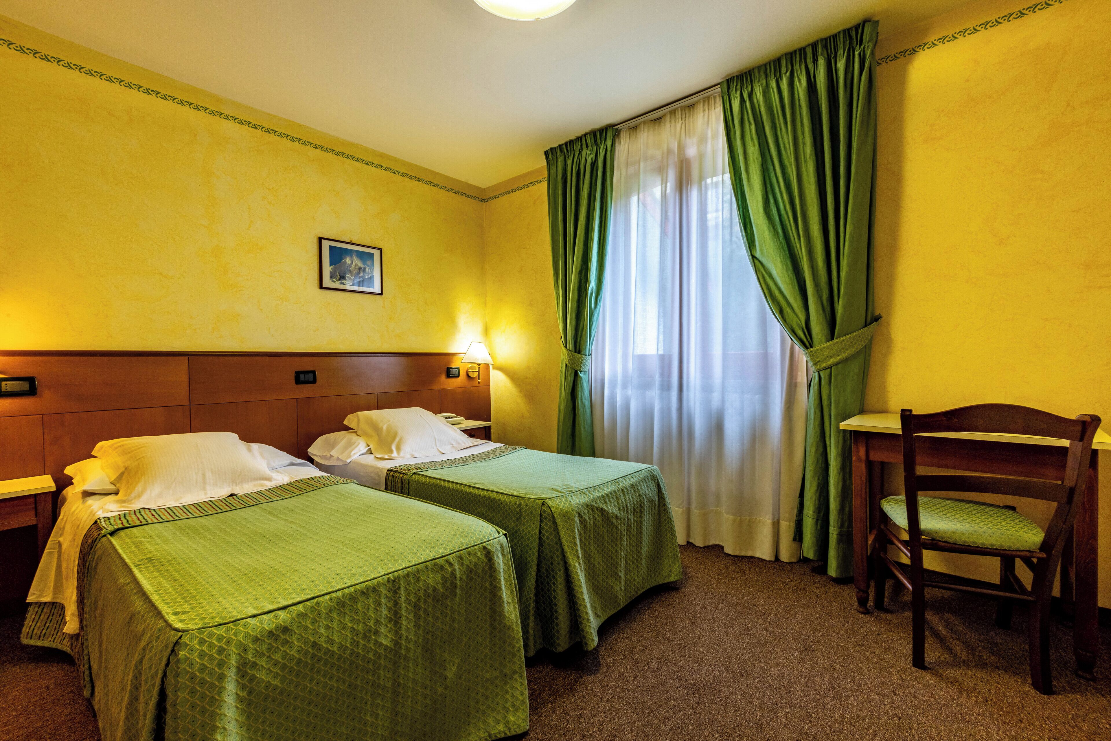 Une chambre d’hôtel avec deux lits, un bureau, une chaise, une table de chevet et une lampe.