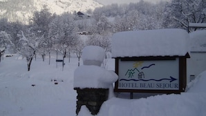 Ein mit Schnee bedecktes Schild für das Hotel Beau Sejour, im Hintergrund eine Berglandschaft.