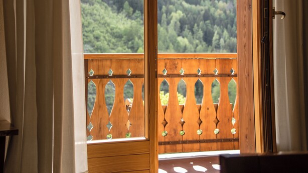 Ein Zimmer mit Holztür und Zugang zu einem Balkon mit Blick auf einen bewaldeten Berg.