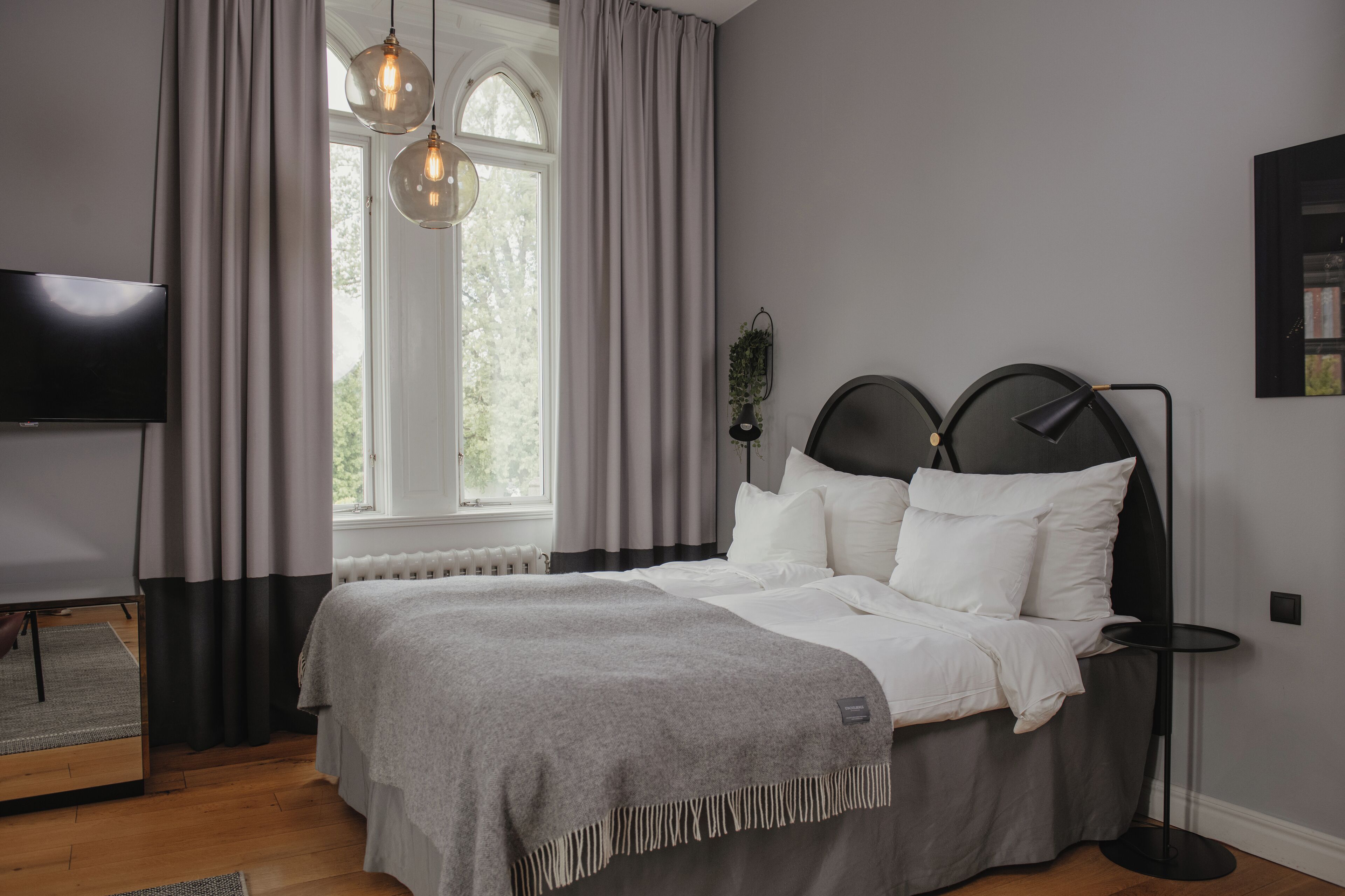 A modern bedroom with a bed, a bedside table, a TV, and a window with curtains.