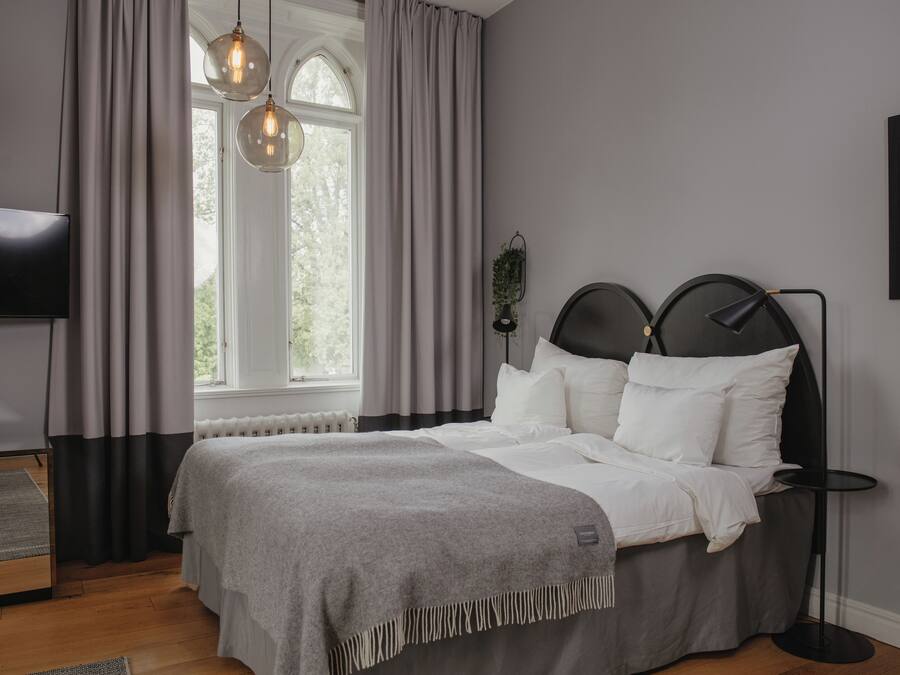 A modern bedroom with a bed, a bedside table, a TV, and a window with curtains.