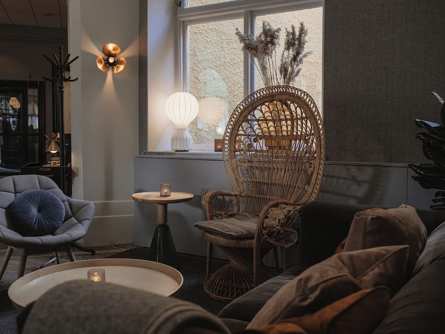 Un coin salon accueillant avec un fauteuil en osier, un fauteuil gris et une petite table ronde sur laquelle est posée une bougie.
