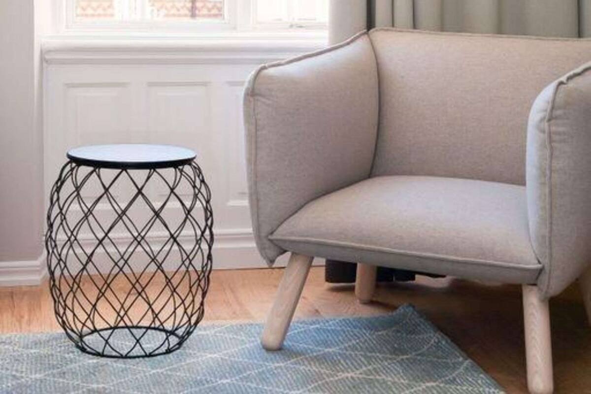 A room with a grey sofa, a round wireframe side table, and a patterned rug.