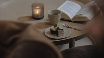 A round wooden table with a candle, a cup, a book, and a plate with a dessert.