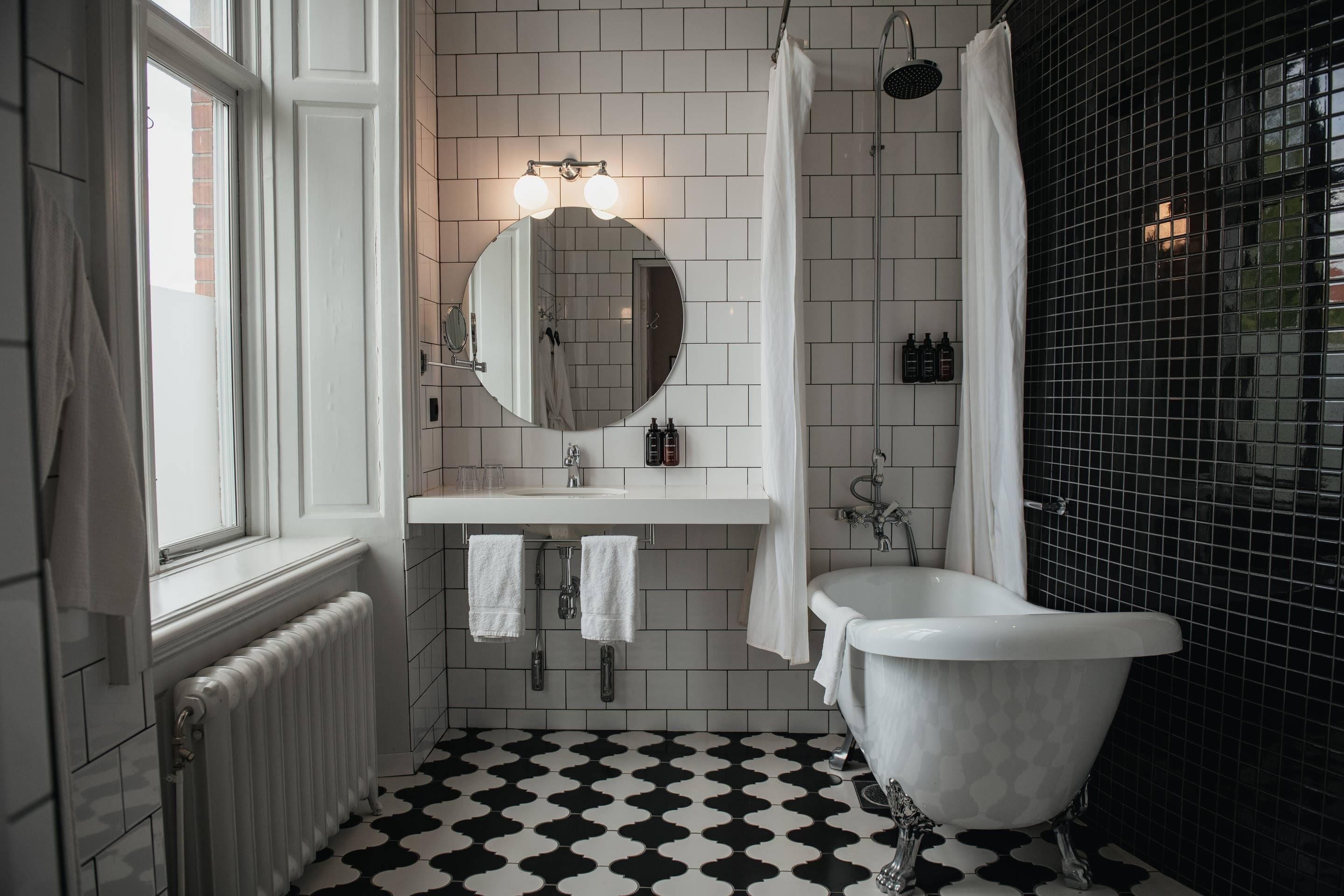A bathroom with a white bathtub, a round mirror, a white sink, and a shower.