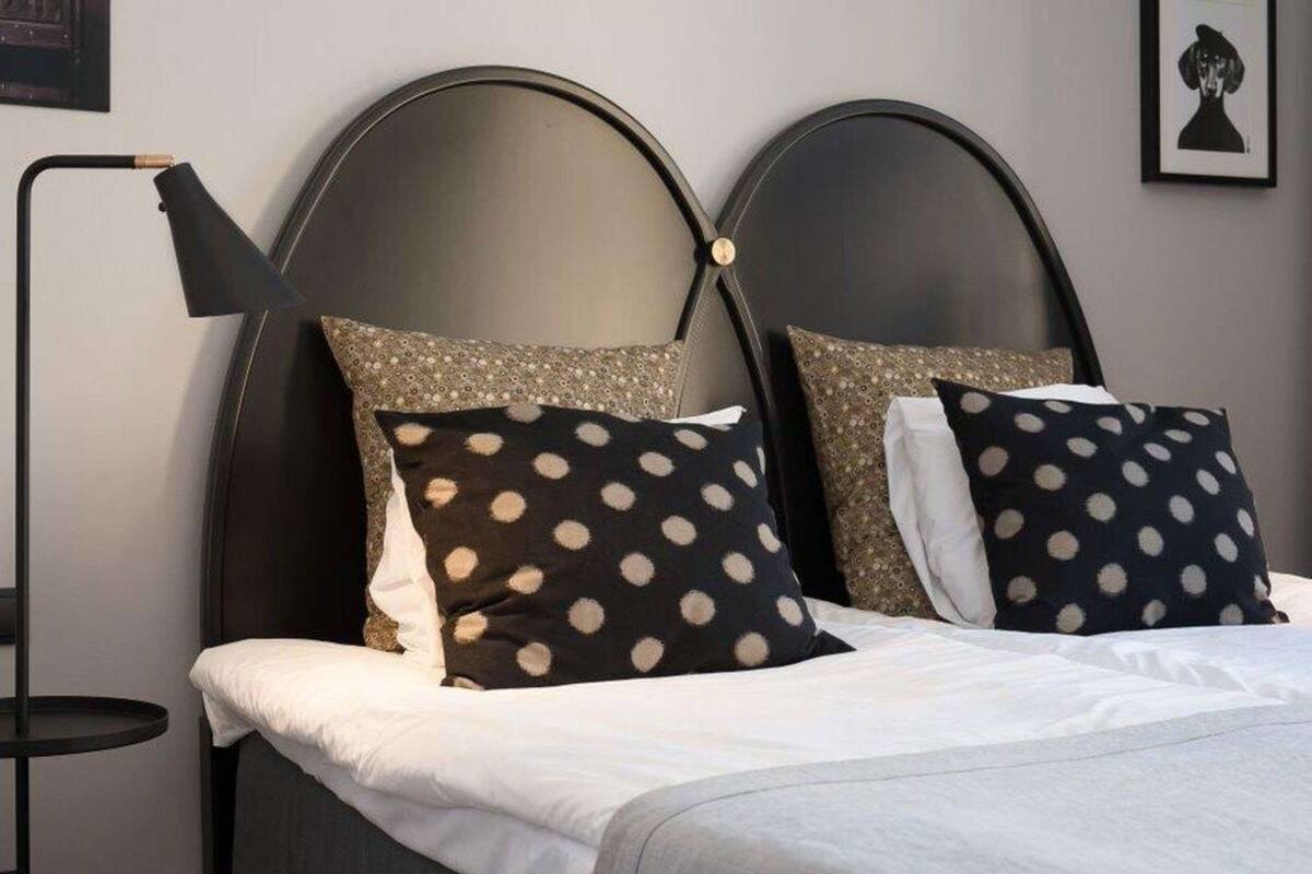 A bed with a headboard, two pillows with polka dot patterns, a bedside lamp, and a framed picture on the wall.