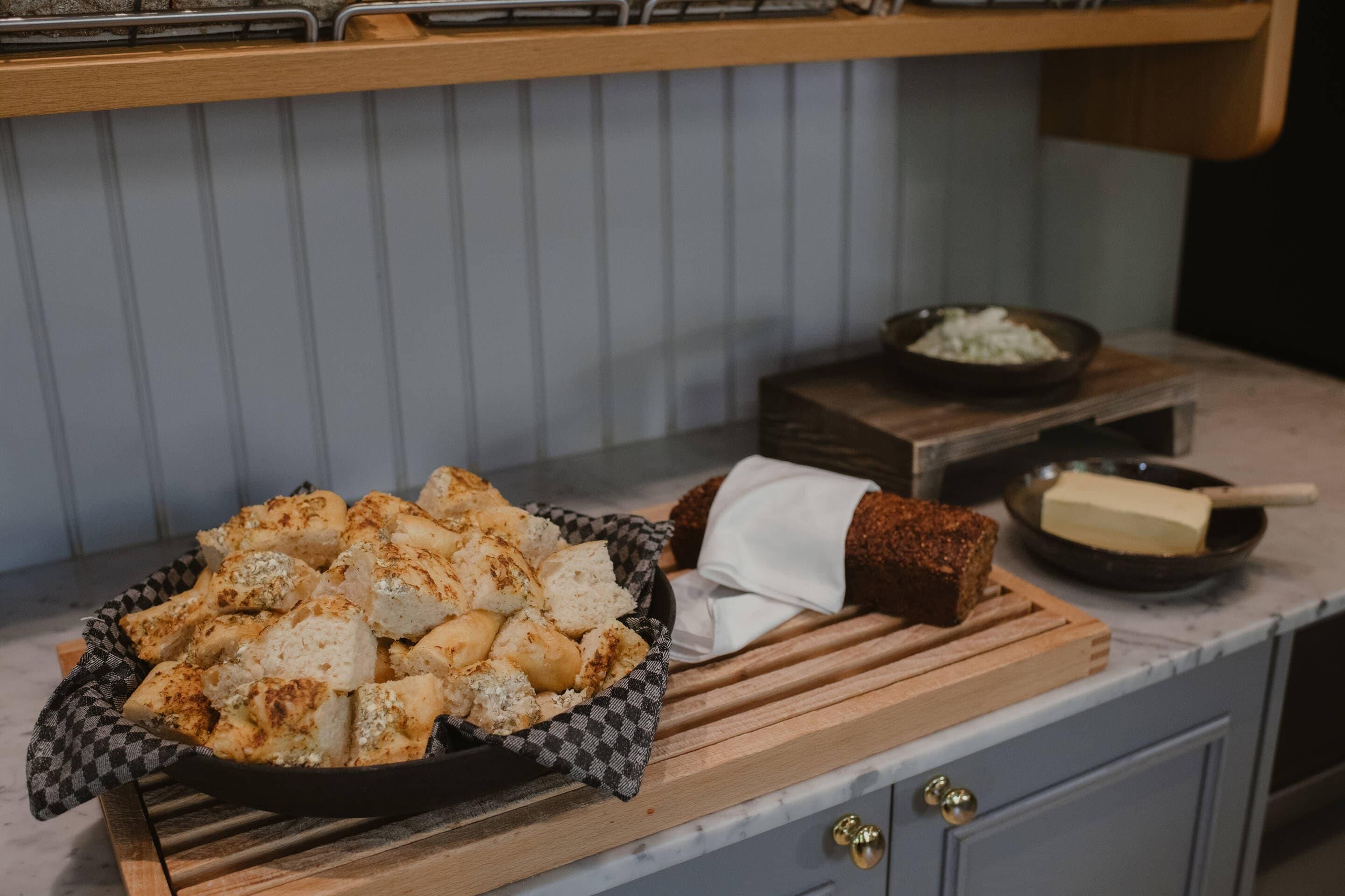 A kitchen counter with a bowl of bread, a wooden cutting board, and a bowl of onions.