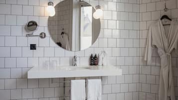 Ein modernes Badezimmer mit weiß gefliesten Wänden, einem runden Spiegel mit Beleuchtung, einem weißen Waschbecken und einem an der Wand hängenden Bademantel.