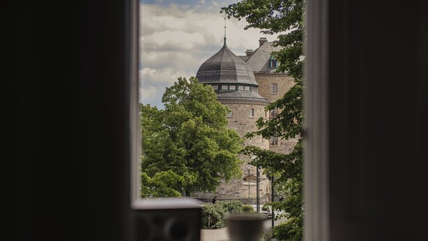 A view of a historic building with a prominent dome and stone walls through a window. - Home Hotel Borgen (Örebro)