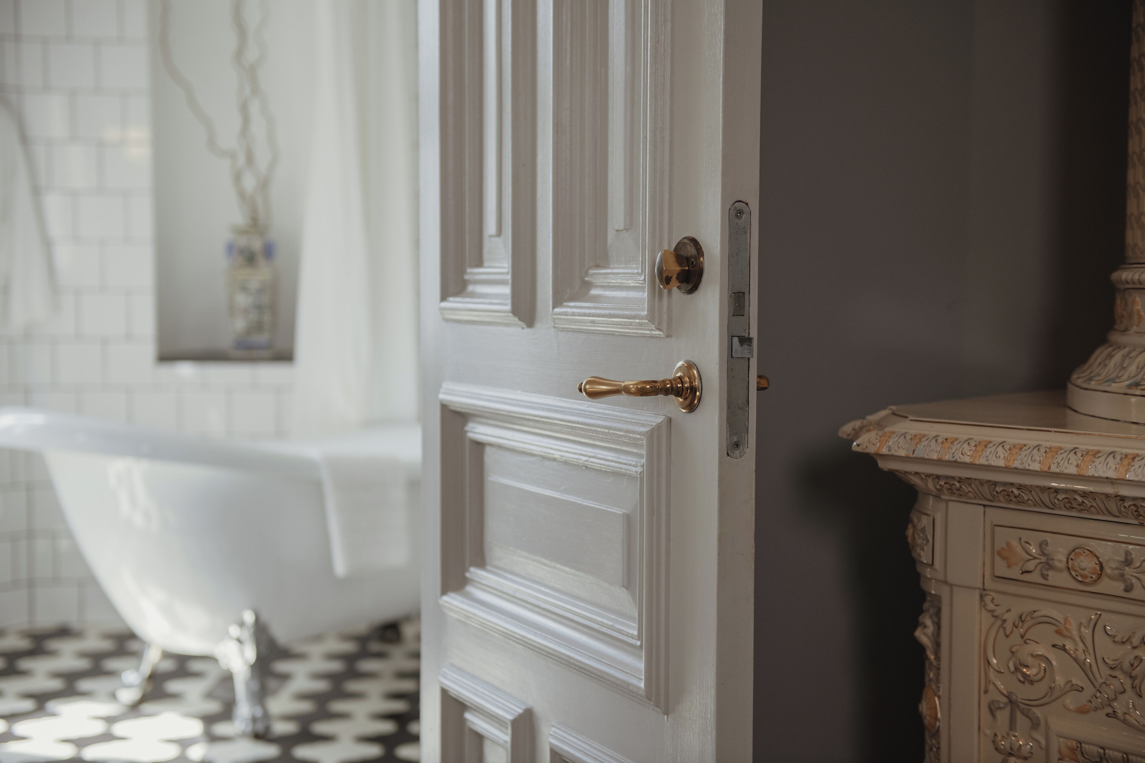 A bathroom with a white bathtub, a white door with a brass doorknob, and a marble vanity with intricate designs.