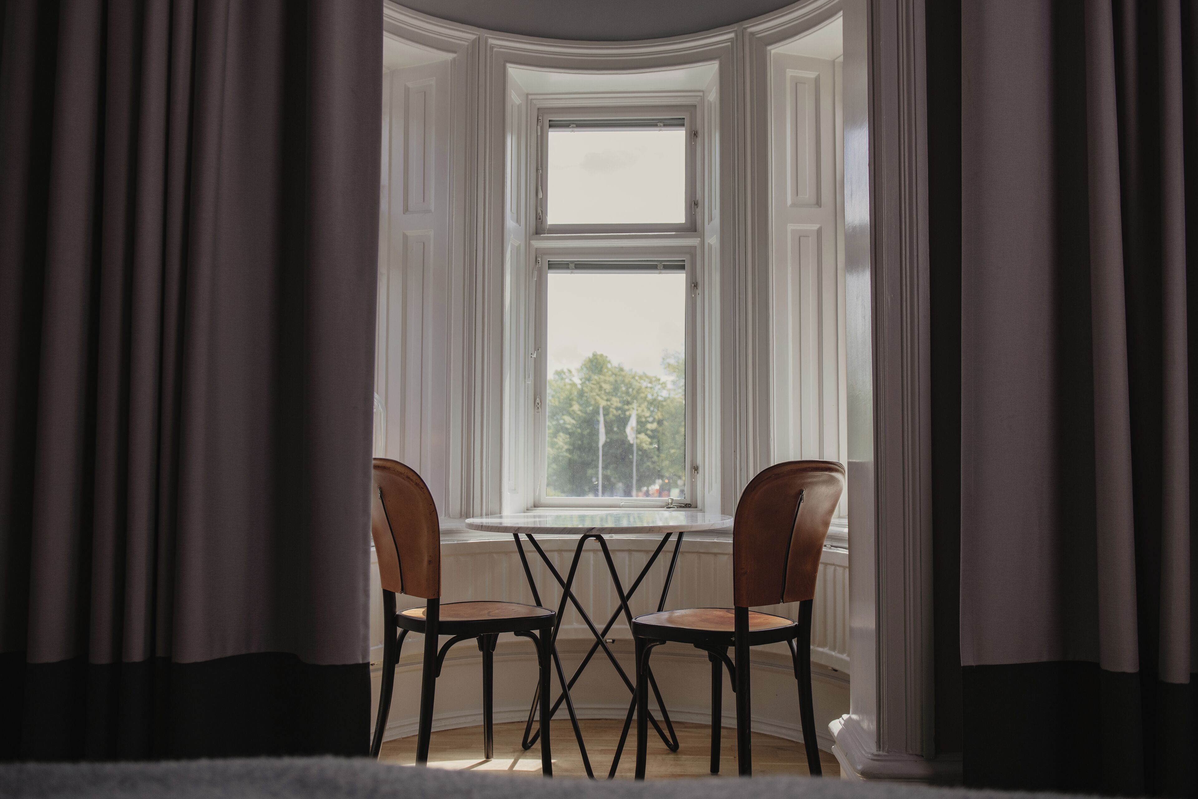 A room with a bay window, two chairs, and a table.