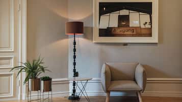 A room with a framed picture of a bar, a floor lamp, a chair, and two potted plants.